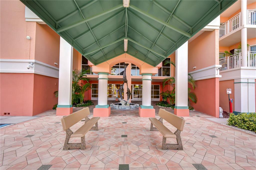 An outdoor covered entrance features a dolphin fountain, two benches, and peach-colored building walls — 4516 SEAGULL DRIVE UNIT 318, NEW PORT RICHEY, FL