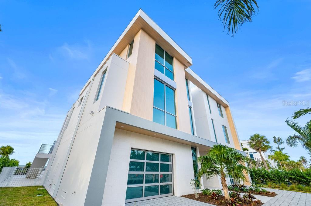A low-angle exterior view of a modern multi-story home with large glass windows and balconies — 6489 GULFSIDE ROAD, LONGBOAT KEY, FL