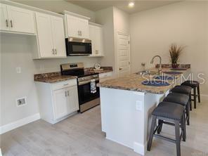 A kitchen with white cabinets, stainless steel appliances, a kitchen island, and bar stools — 231 BITTERN LOOP, INVERNESS, FL