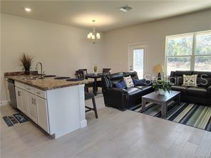 An open-concept living and dining area features a kitchen island, dark leather furniture, and tile flooring — 231 BITTERN LOOP, INVERNESS, FL