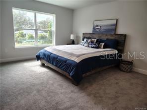 A bedroom features a bed with a wooden headboard, a window, and gray carpeting — 231 BITTERN LOOP, INVERNESS, FL