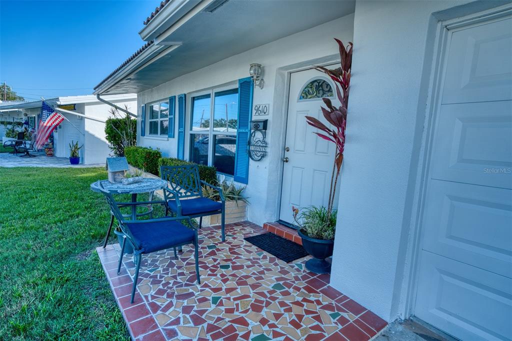 A front porch features a mosaic tile floor, two chairs, a small table, and a door — 9610 45TH STREET N, PINELLAS PARK, FL