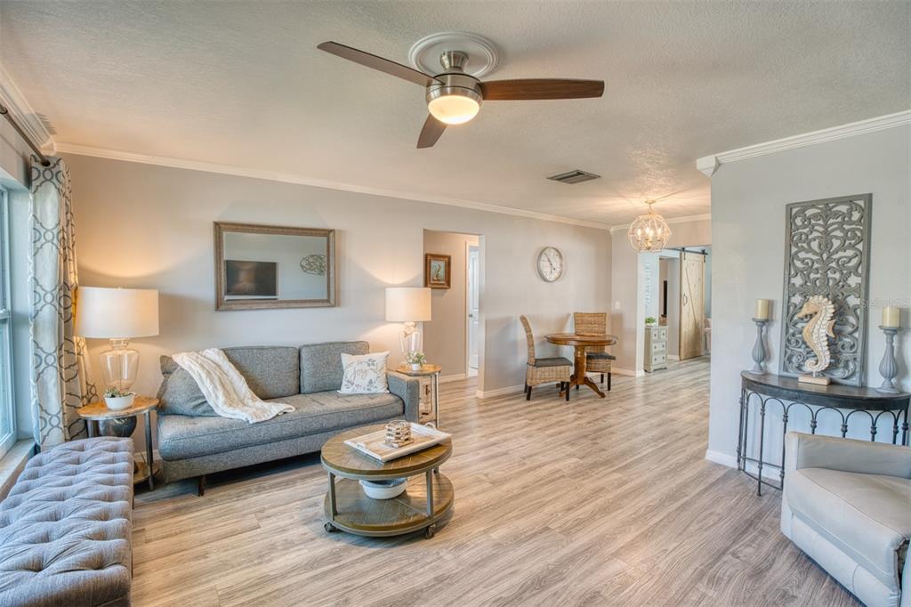 A living room features a gray sofa, a round coffee table, and light wood-look flooring — 9610 45TH STREET N, PINELLAS PARK, FL