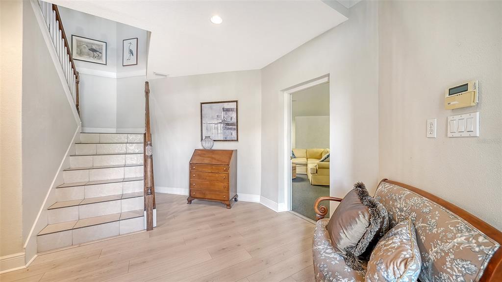 A foyer features tiled stairs, light wood-look flooring, a wooden secretary desk, and a loveseat — 12402 HARBOUR LANDINGS DRIVE, CORTEZ, FL