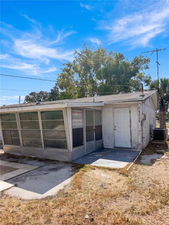 The exterior of a small, white, single-story house features a screened-in porch and a patio — 2412 ARCADIA ROAD, HOLIDAY, FL