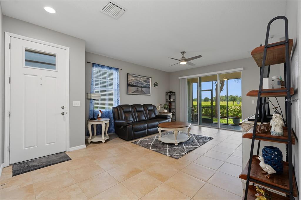 A living room with tile floors, a black leather sofa, a television, and sliding glass doors — 33067 WINDELSTRAW DRIVE, WESLEY CHAPEL, FL