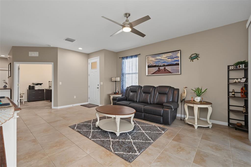 A living room with tile floors, a ceiling fan, and an open view to the kitchen — 33067 WINDELSTRAW DRIVE, WESLEY CHAPEL, FL