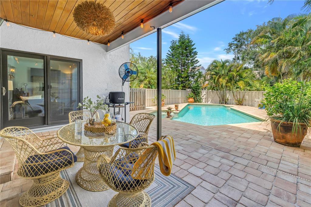 A covered patio features a glass-topped dining set, a swimming pool, and tropical landscaping — 990 SAN CARLOS COURT NE, ST PETERSBURG, FL