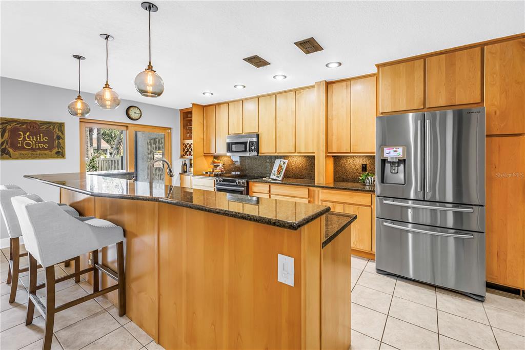 A kitchen features light wood cabinets, granite countertops, stainless steel appliances, and a breakfast bar — 990 SAN CARLOS COURT NE, ST PETERSBURG, FL