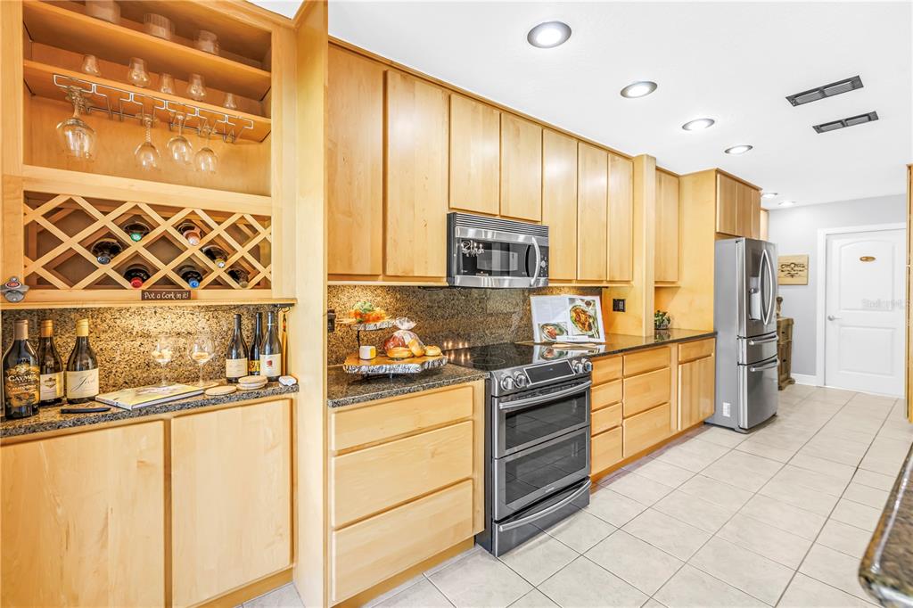 A kitchen features light wood cabinets, granite countertops, stainless steel appliances, and a wine rack — 990 SAN CARLOS COURT NE, ST PETERSBURG, FL