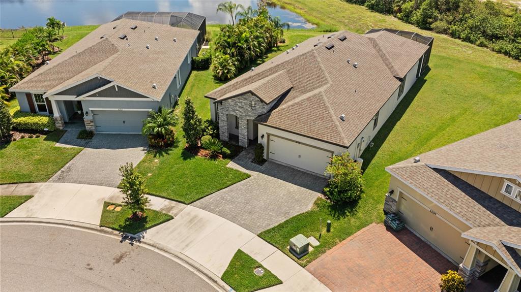 An aerial view shows three suburban houses with paved driveways and manicured lawns near a pond — 6211 SEA AIR DRIVE, APOLLO BEACH, FL