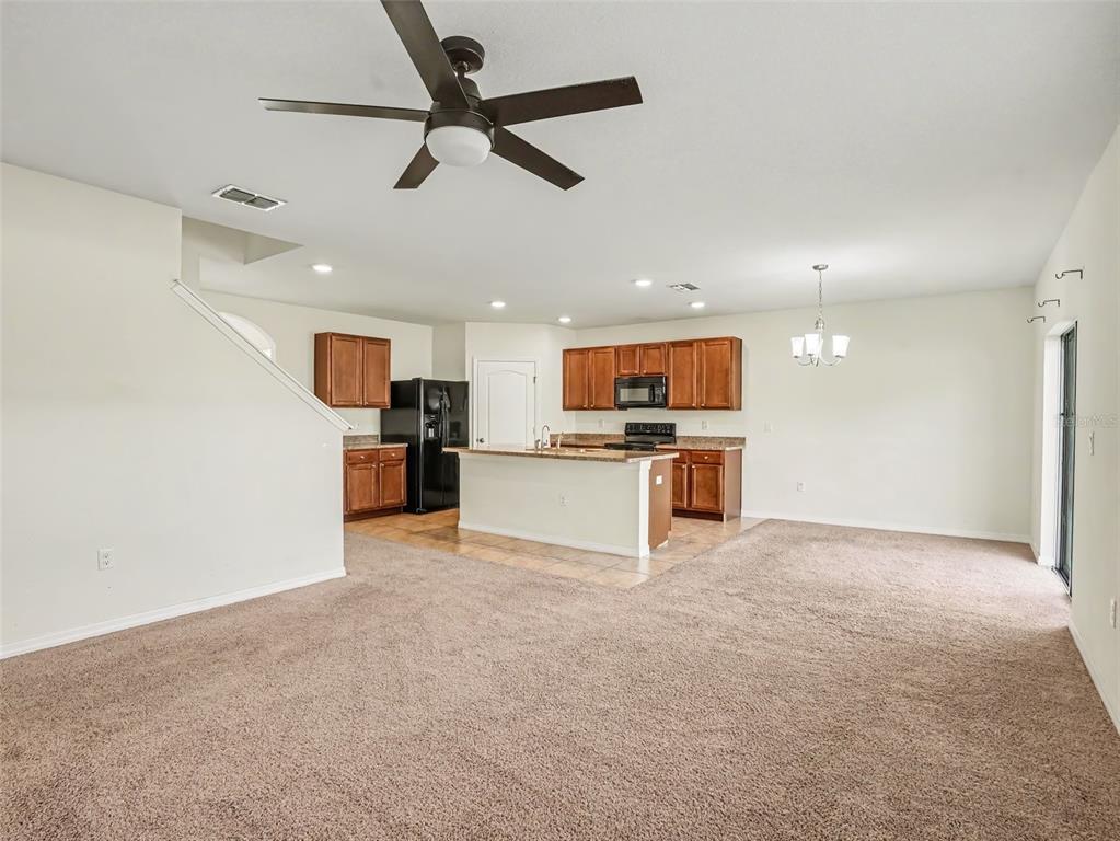 An open-concept kitchen with brown cabinets, a central island, and tile flooring next to carpet — 281 ST GEORGES CIRCLE, EAGLE LAKE, FL