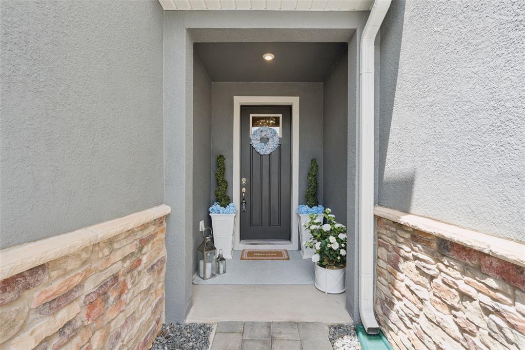 A front entryway features a dark gray door, stone siding, and potted topiary plants — 896 SPRING PALMS LOOP, ORLANDO, FL