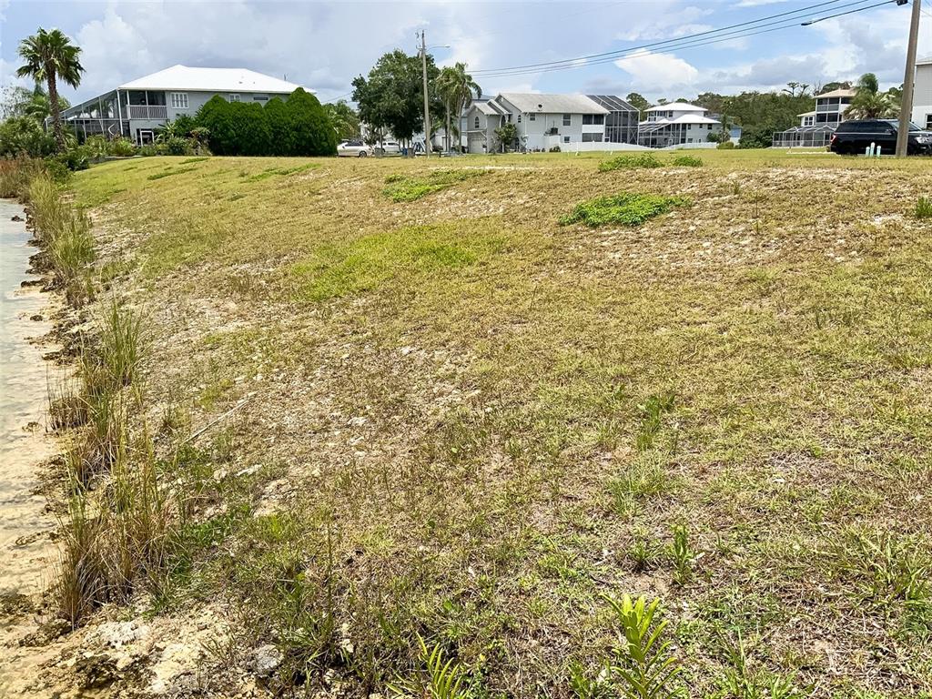 A grassy, sloped waterfront lot sits in front of several residential houses — 3471 CROAKER DRIVE, HERNANDO BEACH, FL