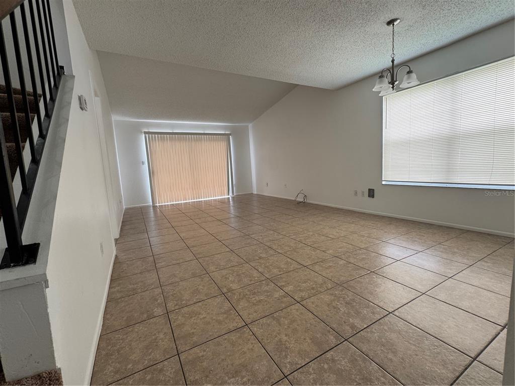 An empty living room features tiled floors, a vaulted ceiling, and a sliding glass door — 2352 PEBBLE BROOK ROAD, KISSIMMEE, FL