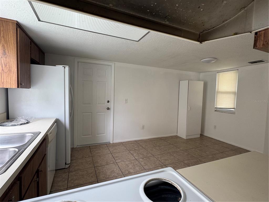 A kitchen with wood cabinets, white appliances, tile flooring, and a white door — 2352 PEBBLE BROOK ROAD, KISSIMMEE, FL