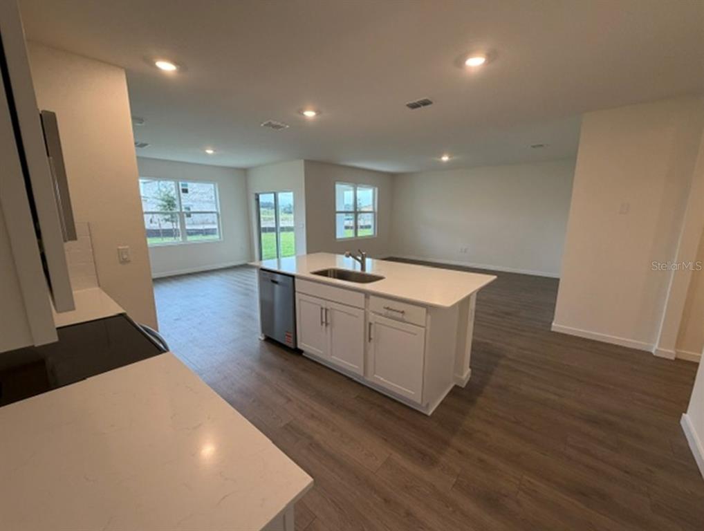 An open-concept living area with light wood-look flooring, a kitchen island, and sliding glass doors — 4922 MARSHELDER STREET, APOPKA, FL