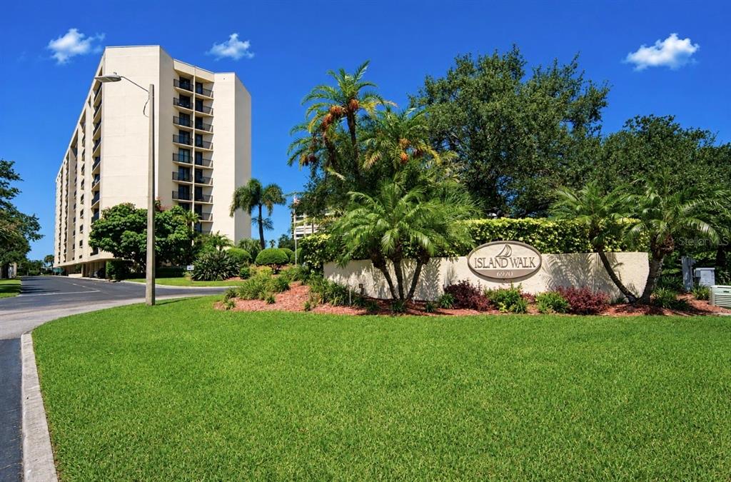 A multi-story residential building stands behind a landscaped sign for Island Walk — 690 ISLAND WAY UNIT 501, CLEARWATER BEACH, FL