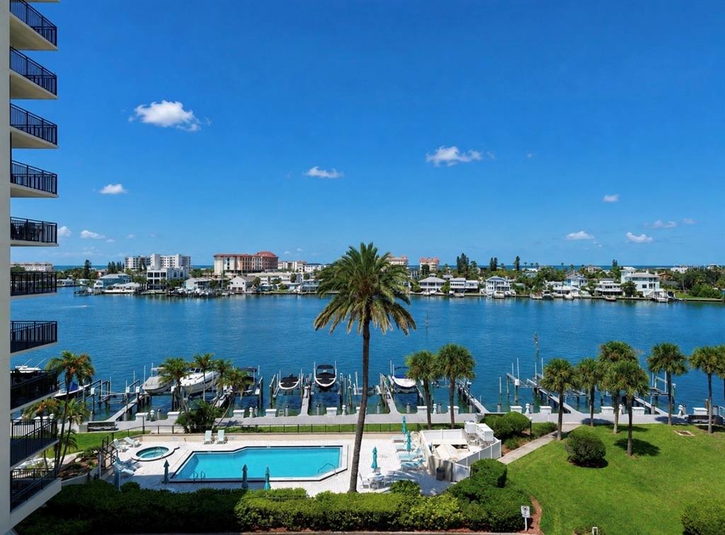 An elevated view of a swimming pool, boat docks, and a waterway with distant buildings — 690 ISLAND WAY UNIT 501, CLEARWATER BEACH, FL