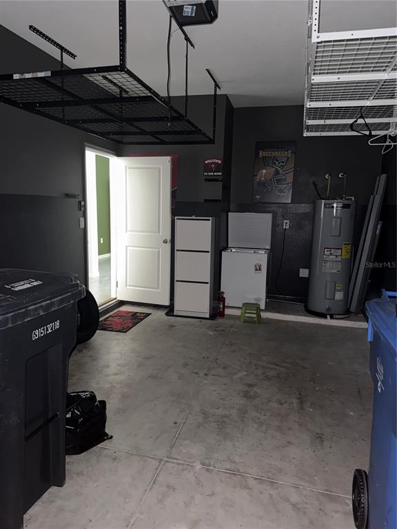 A garage with dark walls, overhead storage racks, a water heater, and a chest freezer — 191 MANGROVE SHADE CIRCLE, APOLLO BEACH, FL