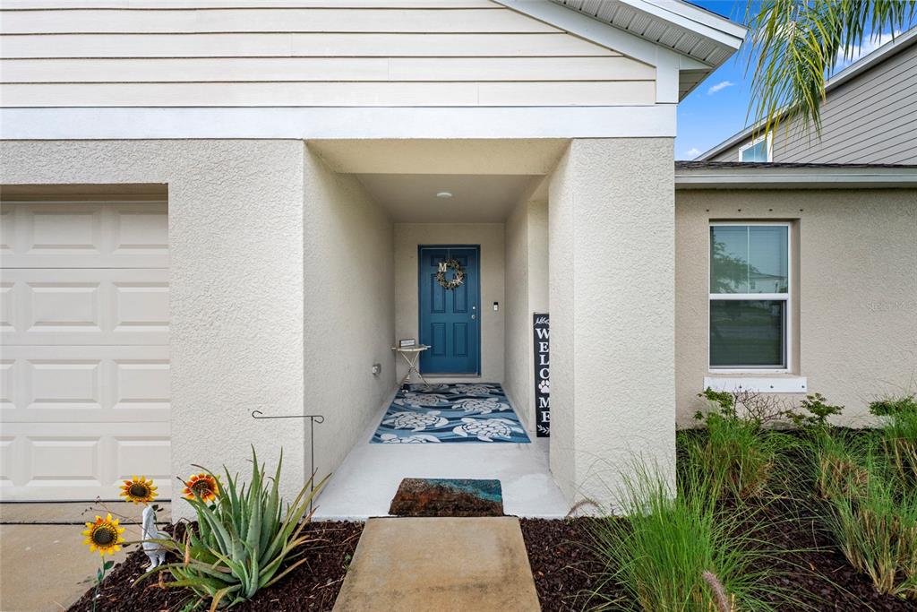 The exterior of a house features a blue front door, a welcome sign, and landscaping — 12690 TANNENCREST DRIVE, RIVERVIEW, FL