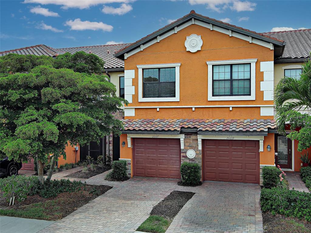 A two-story townhouse with an orange stucco facade, two garage doors, and a paver driveway — 20217 LAGENTE CIRCLE, VENICE, FL