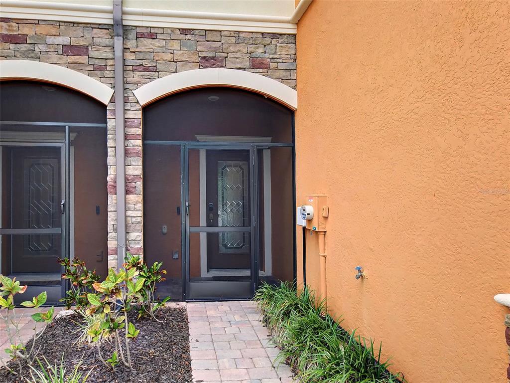 A stone-accented entryway features a screened door, a paved walkway, and an orange stucco wall — 20217 LAGENTE CIRCLE, VENICE, FL