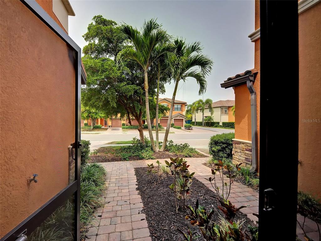 A view from a doorway looking out onto a brick walkway, palm trees, and neighborhood homes — 20217 LAGENTE CIRCLE, VENICE, FL