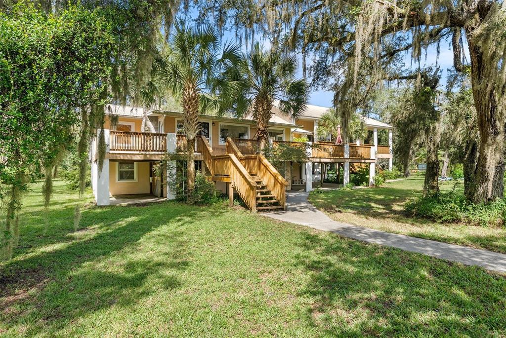 A two-story house with a wooden deck, staircase, and palm trees in a grassy yard — 2033 SE HIGHWAY 317, OLD TOWN, FL