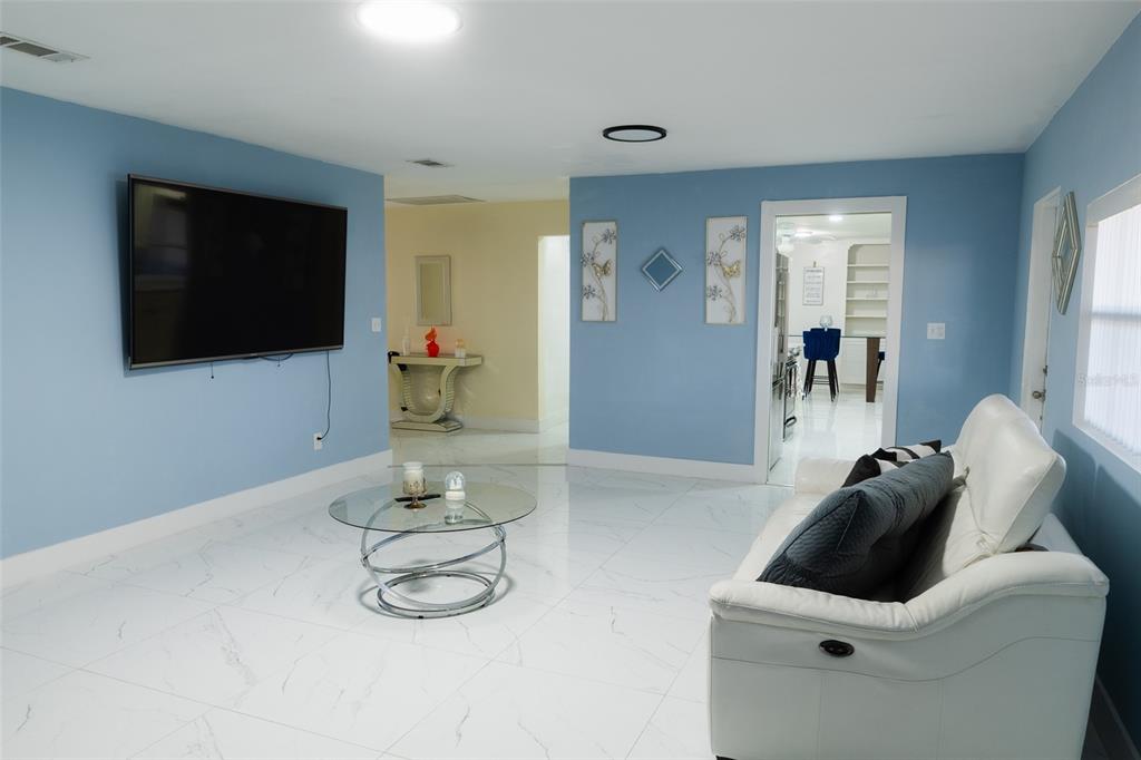 A living room with light blue walls, white tile flooring, a white sofa, and a television — 4710 SHALE PLACE, TAMPA, FL