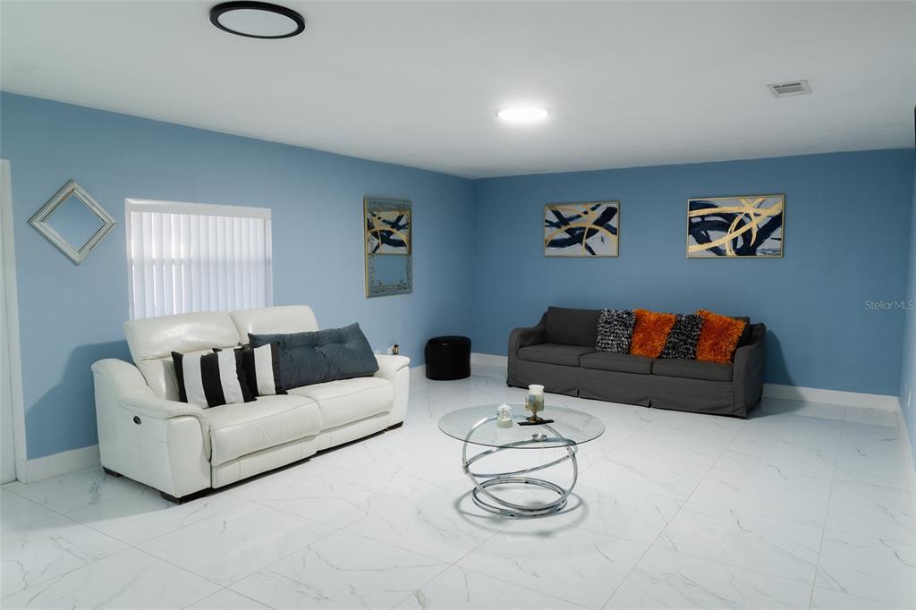 A living room features blue walls, white tile flooring, a white sofa, and a gray sofa — 4710 SHALE PLACE, TAMPA, FL
