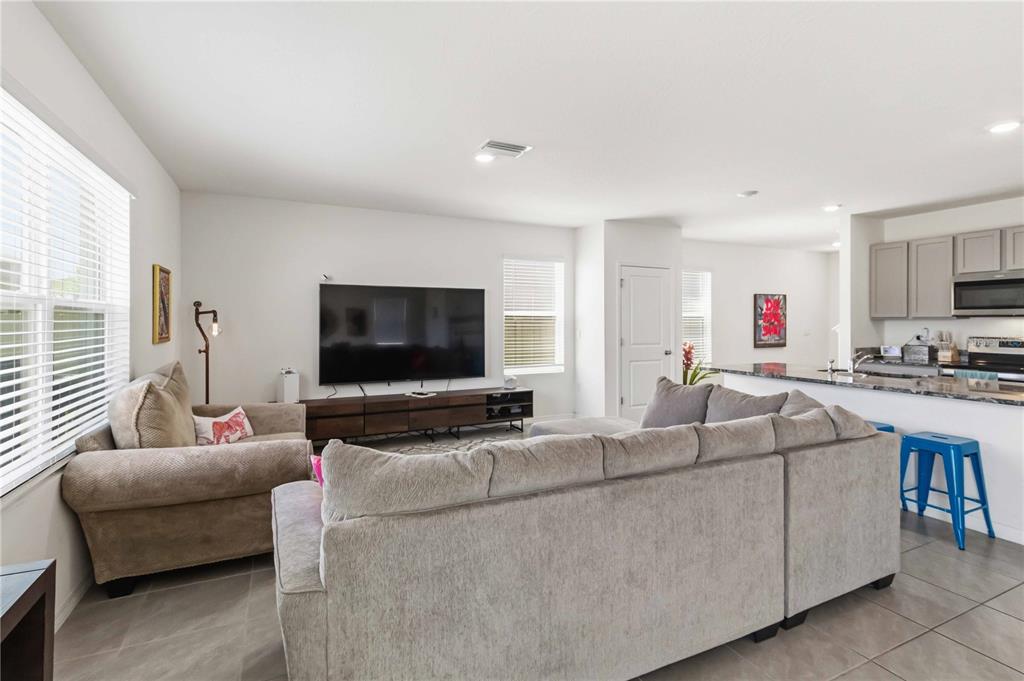 A living room features a grey sectional sofa, a television on a console, and kitchen — 8354 HARDY BAY LOOP, WESLEY CHAPEL, FL