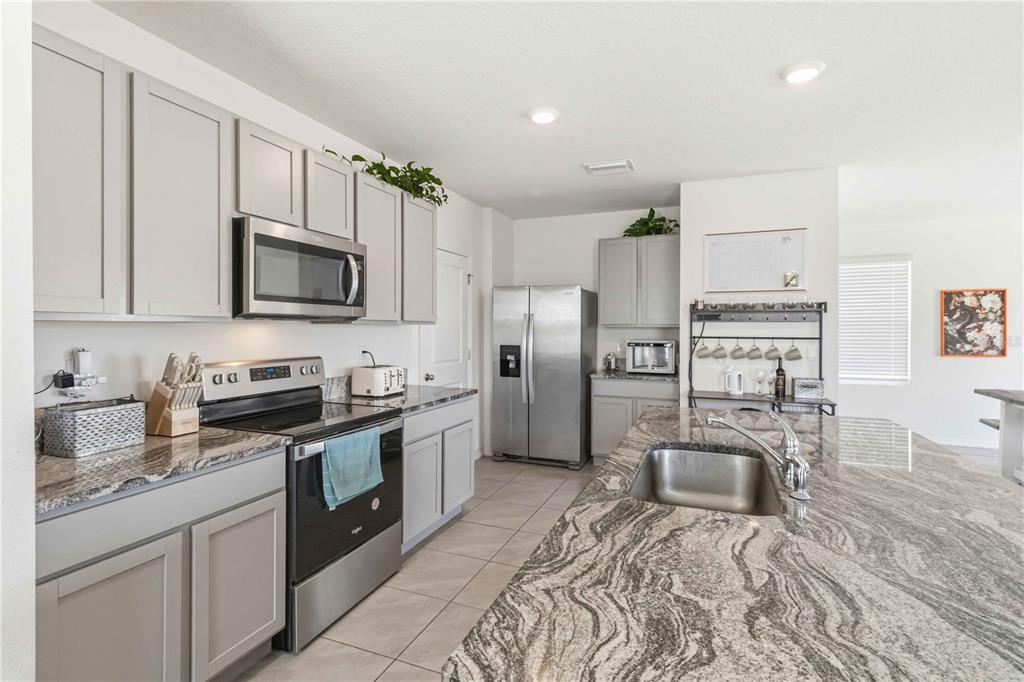 A kitchen features gray cabinets, granite countertops, stainless steel appliances, and a large center island — 8354 HARDY BAY LOOP, WESLEY CHAPEL, FL
