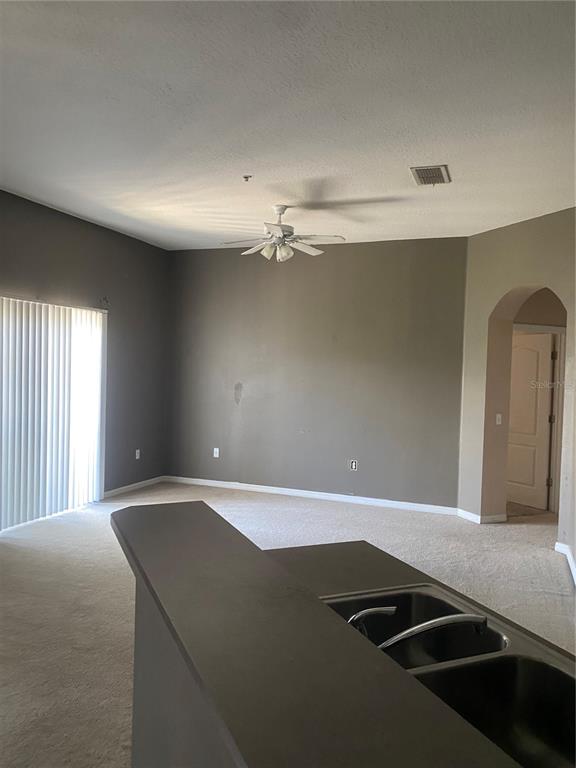 A kitchen sink overlooks a carpeted living room with a ceiling fan and sliding glass doors — 3537 CLAY BRICK ROAD UNIT 3537, HARMONY, FL