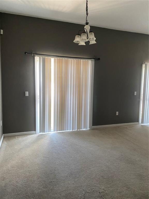 A room with dark gray walls, beige carpeting, a chandelier, and vertical sliding glass doors — 3537 CLAY BRICK ROAD UNIT 3537, HARMONY, FL