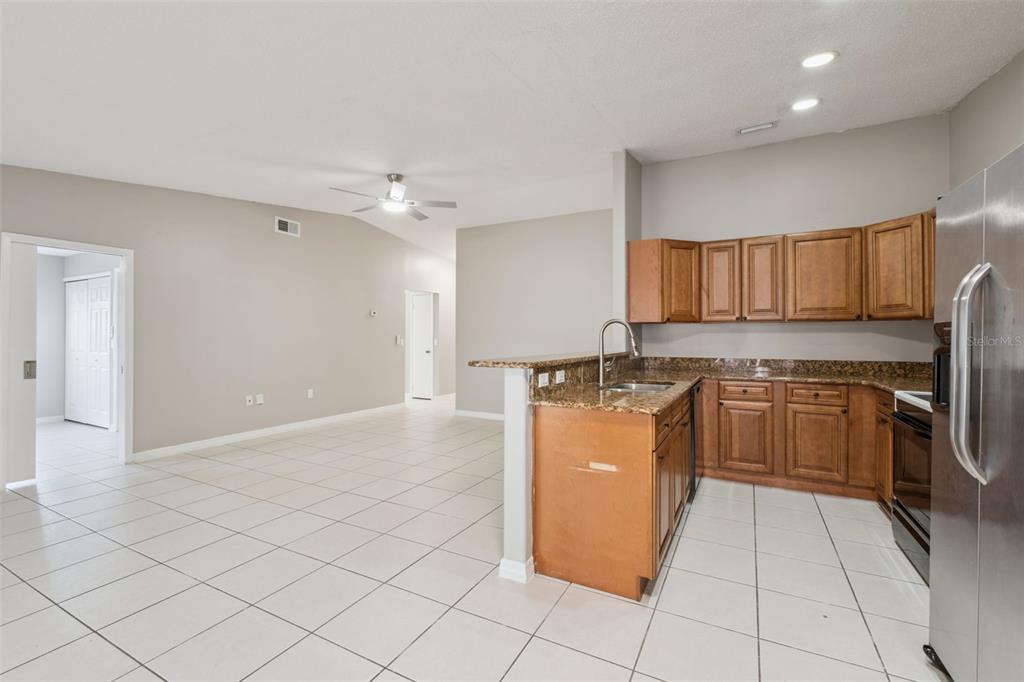 A kitchen features wood cabinets, granite countertops, a stainless steel refrigerator, and a black stove — 3122 LORRY LANE, ORLANDO, FL