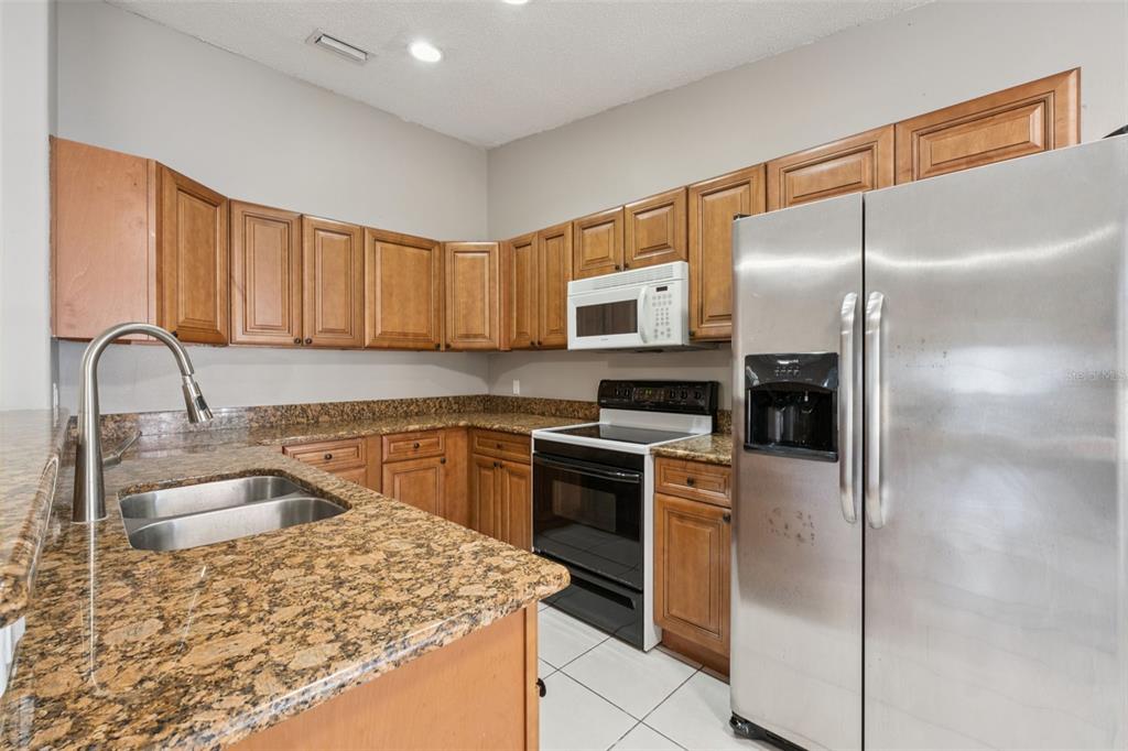 A kitchen features wood cabinets, granite countertops, a double sink, and white tile flooring — 3122 LORRY LANE, ORLANDO, FL