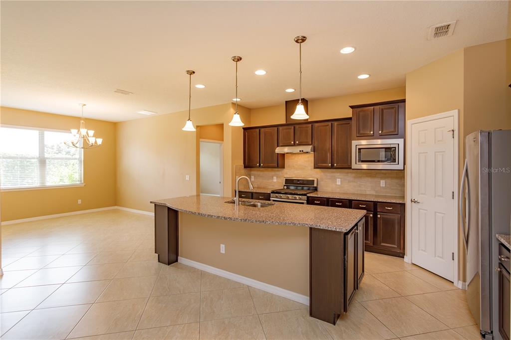 A kitchen features dark wood cabinets, granite countertops, a center island, and tile flooring — 672 CORDOBA DRIVE, DAVENPORT, FL