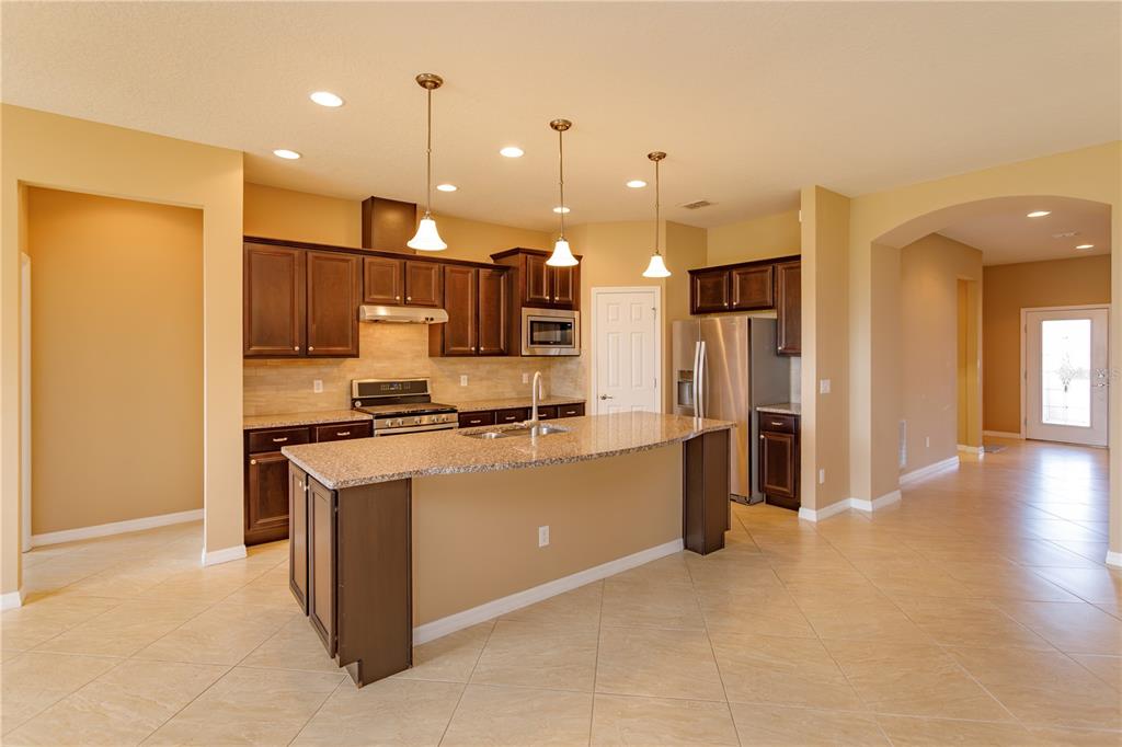 A kitchen with dark wood cabinets, granite countertops, a central island, and light tile flooring — 672 CORDOBA DRIVE, DAVENPORT, FL