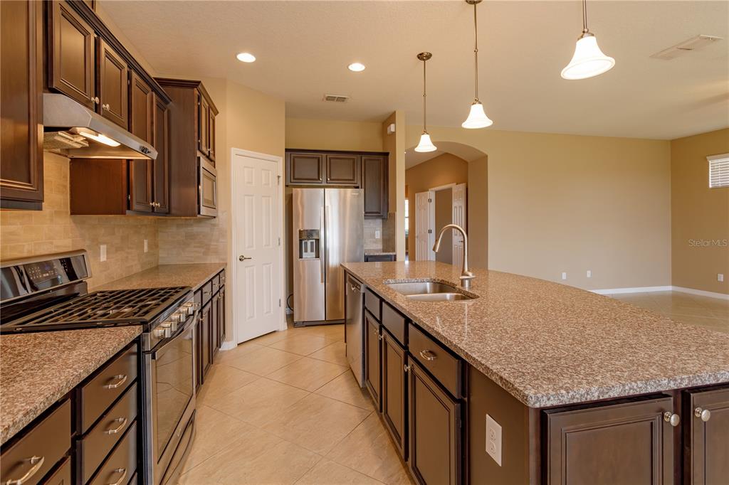 A kitchen with dark wood cabinets, granite countertops, a large island, and stainless steel appliances — 672 CORDOBA DRIVE, DAVENPORT, FL