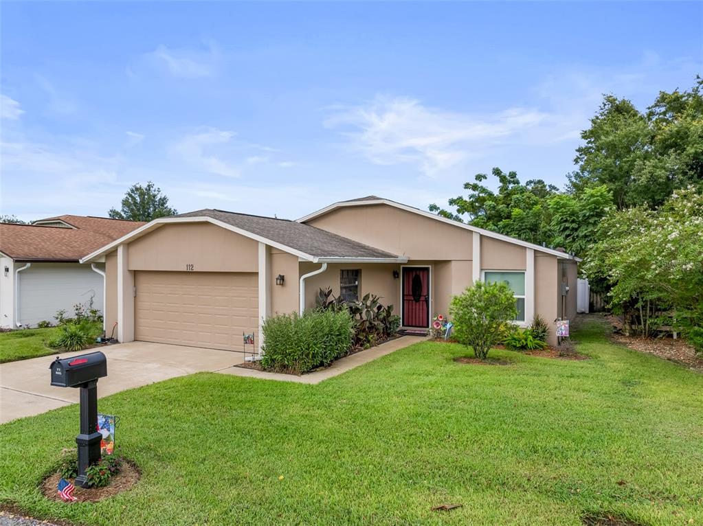 A single-story house with a tan stucco exterior, a two-car garage, and a front lawn — 112 MAYFAIR CT UNIT 112, SANFORD, FL