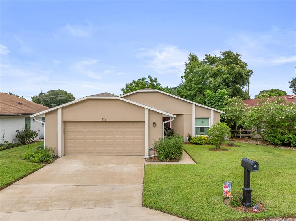 A single-story house with a beige exterior, a two-car garage, and a front lawn — 112 MAYFAIR CT UNIT 112, SANFORD, FL