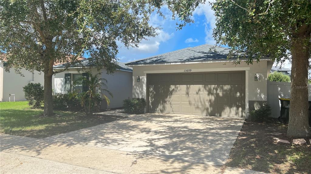 A single-story house with a two-car garage and a concrete driveway under large trees — 13609 LARANJA STREET, CLERMONT, FL