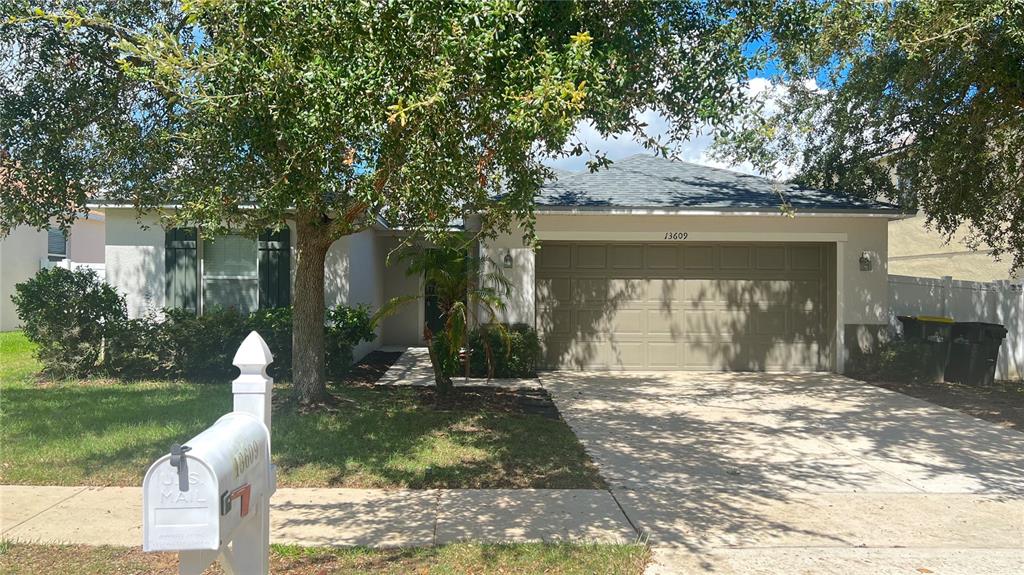 A single-story house with a beige exterior, a two-car garage, and a large front tree — 13609 LARANJA STREET, CLERMONT, FL