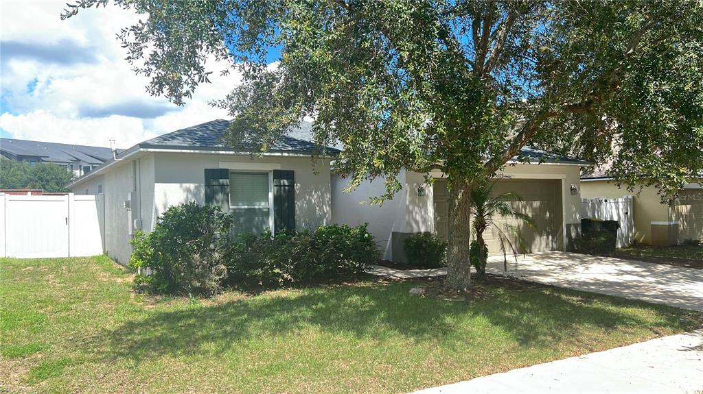 A single-story house with a tan exterior, a two-car garage, and a front yard tree — 13609 LARANJA STREET, CLERMONT, FL