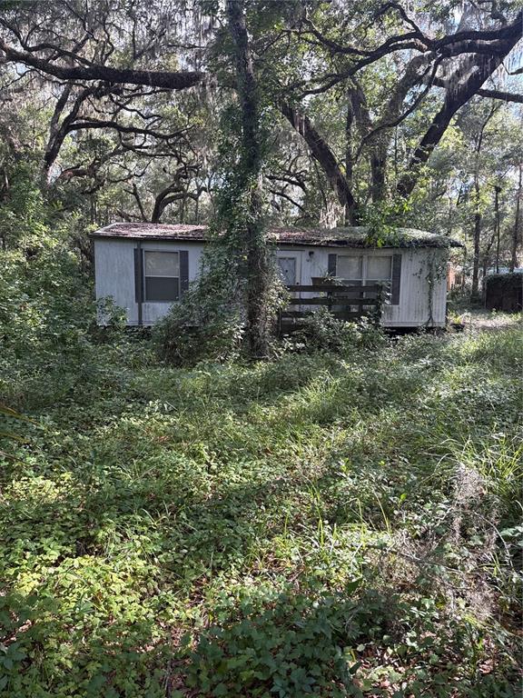 A weathered mobile home sits in a heavily overgrown, wooded lot with a small wooden porch — 5612 E HIGHWAY 316, CITRA, FL
