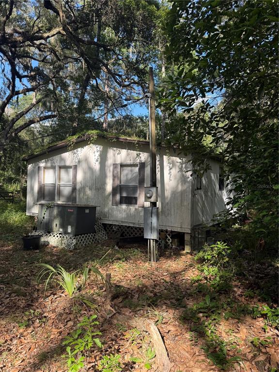 An exterior view of a weathered mobile home surrounded by trees and overgrown vegetation — 5612 E HIGHWAY 316, CITRA, FL