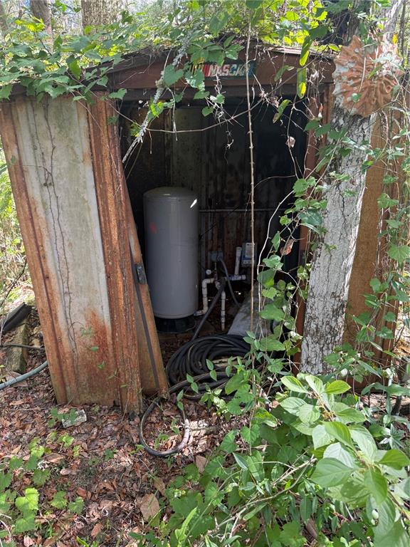 A weathered metal shed houses a water pressure tank and plumbing equipment in a wooded area — 5612 E HIGHWAY 316, CITRA, FL
