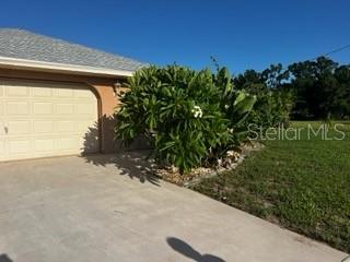 A beige house exterior with a garage and a large green shrub in the front yard — 7506 SPINNAKER BOULEVARD, ENGLEWOOD, FL