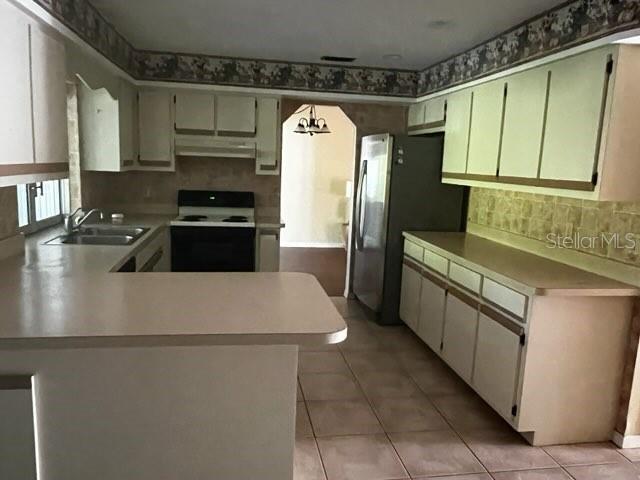 A kitchen features white cabinets, laminate countertops, a stainless steel refrigerator, and tiled flooring — 7506 SPINNAKER BOULEVARD, ENGLEWOOD, FL